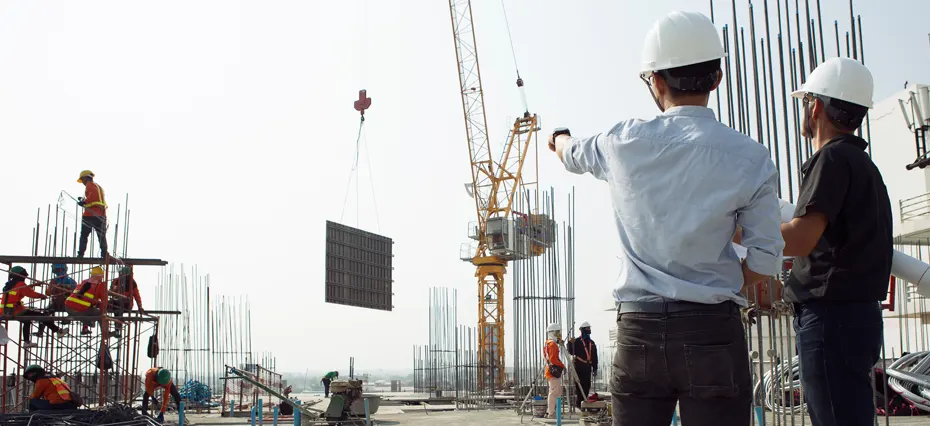 Profissionais de construção civil e engenheiros realizando prospecção de obras em construção com uso de capacetes e equipamentos de segurança no canteiro.